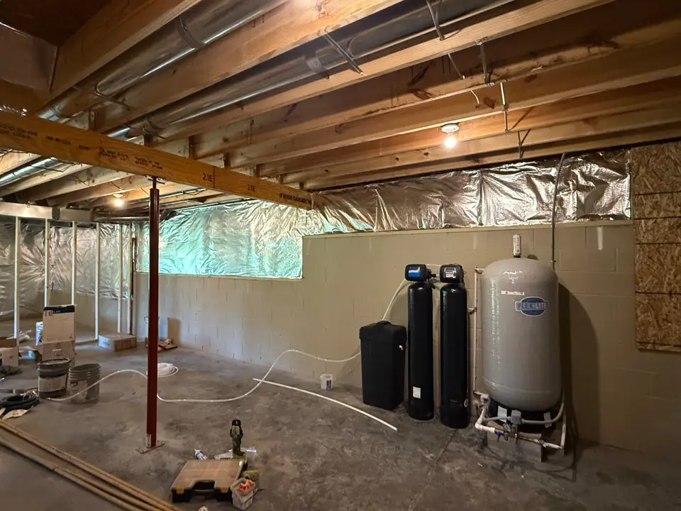 A finished water treatment install in a basement: a softener, two filter tanks and a large pressure tank against the wall