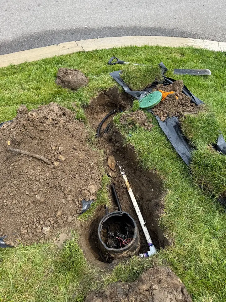A trench dug through a lawn to a valve box, with black poly line exposed for repair