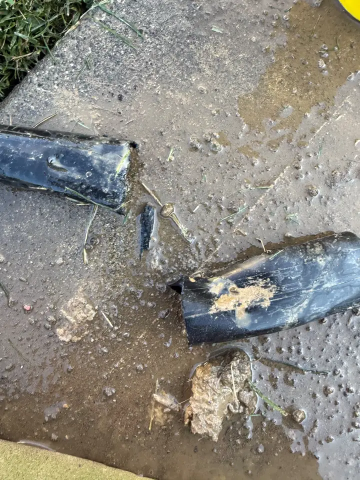 A split black poly pipe lying on wet concrete after being cut out