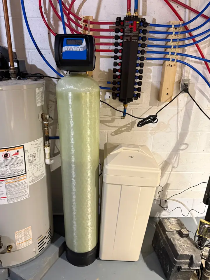 A water softener with a brine tank and a tall filter tank installed beside a water heater